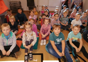 Dzieci siedzą na podłodze i słuchają bajki opowiadanej przez aktorkę